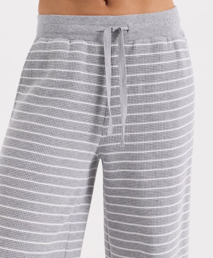 Close-up of a person wearing gray waffle-knit pants with thin white horizontal stripes and a matching gray drawstring waistband.