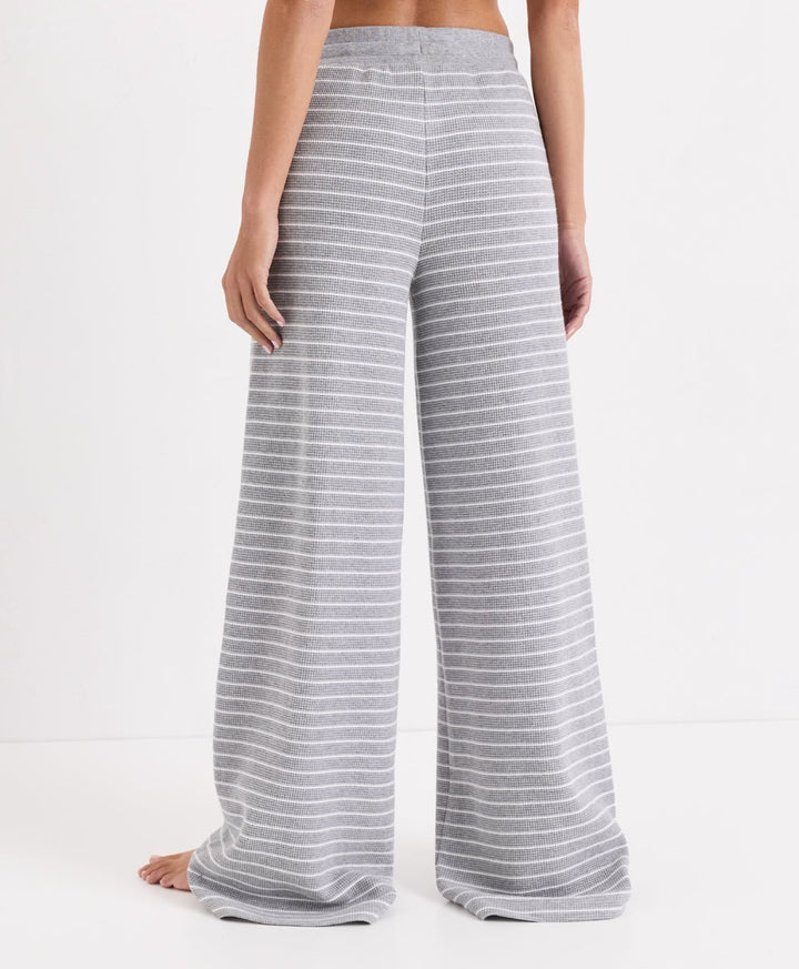 A person shown from the back wearing high-waisted, wide-leg lounge pants with thin gray and white horizontal stripes, photographed against a clean white studio background.