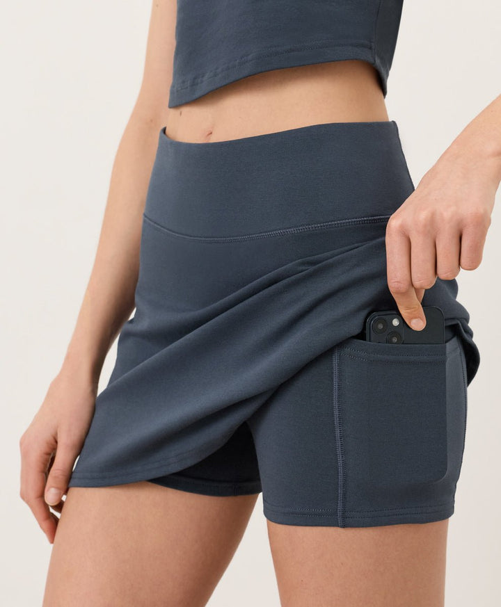 Woman wearing a steel blue Pact skort on a plain background