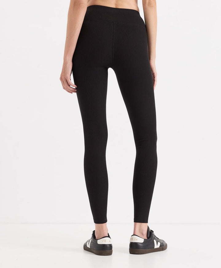 A model from the back wearing black high-waisted leggings and black sneakers with white accents, set against a plain white studio background.