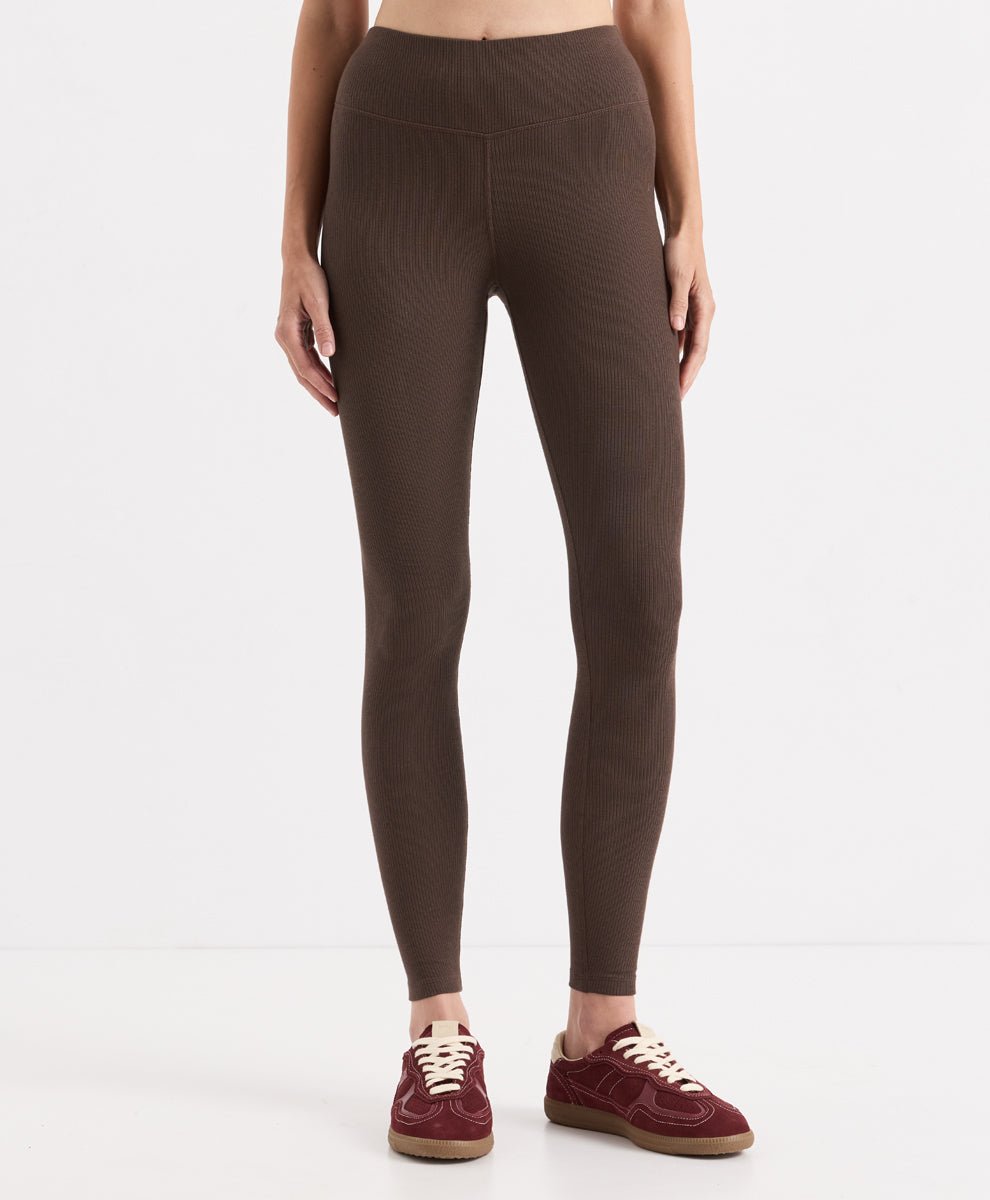 A model from the waist down wearing cocoa ribbed high-waisted leggings and burgundy sneakers, photographed against a clean white studio background.