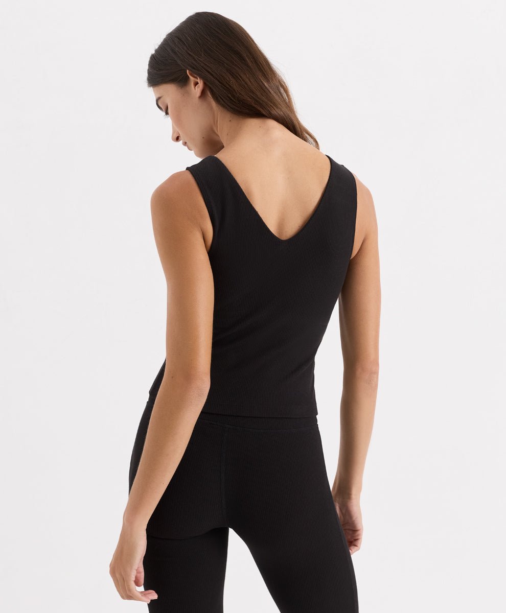 A woman shown from the back wearing a black sleeveless athletic top with a wide scoop neckline and black leggings, photographed against a clean light gray studio background.