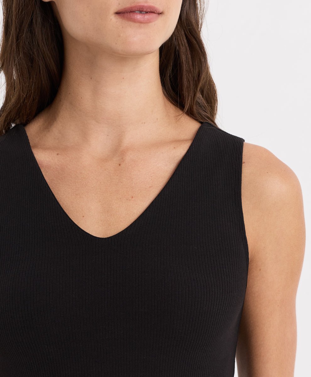 Close-up of a woman wearing a black ribbed sleeveless tank top with a deep V-neckline against a plain light background.