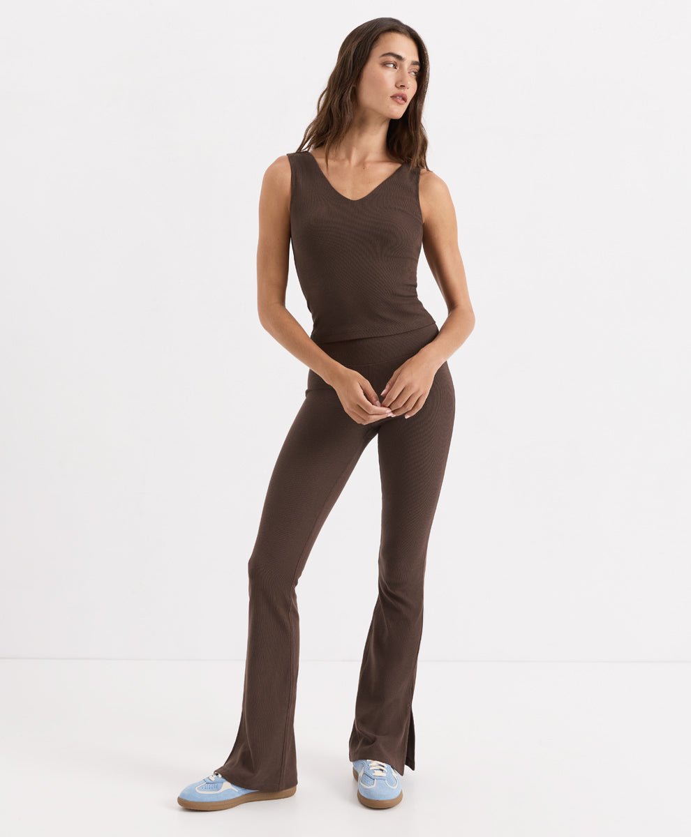 A woman modeling a cocoa ribbed knit tank with a V-neckline and flared leggings, paired with light blue sneakers, against a plain white studio background.