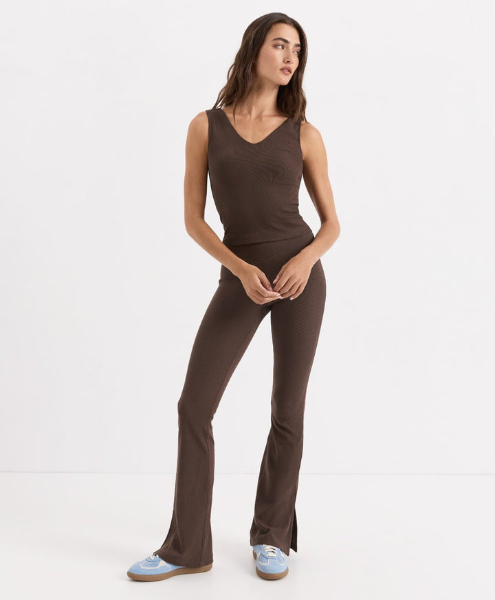 A woman modeling a cocoa ribbed knit tank with a V-neckline and flared leggings, paired with light blue sneakers, against a plain white studio background.