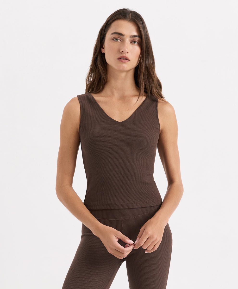 A woman modeling a sleeveless V-neck athletic tank top in cocoa, paired with matching leggings, against a clean white studio background.