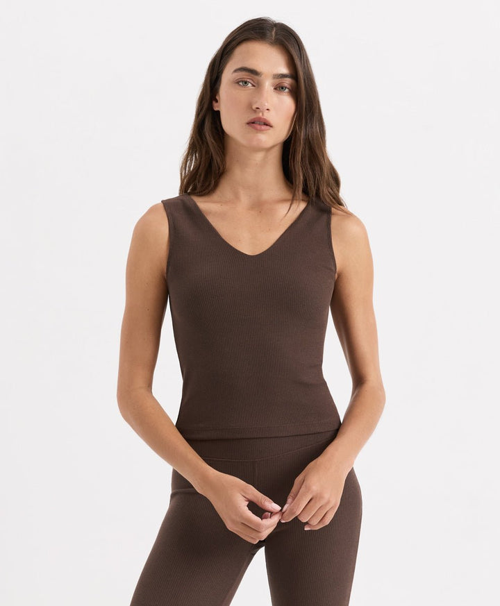 A woman modeling a sleeveless V-neck athletic tank top in cocoa, paired with matching leggings, against a clean white studio background.