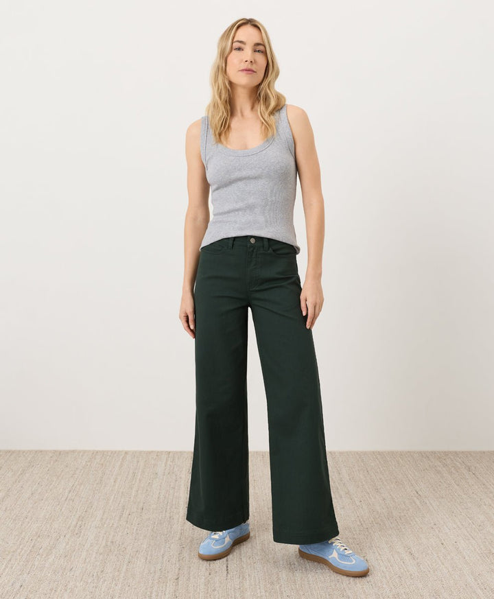Woman wearing a gray tank top and dark green pants against a white background