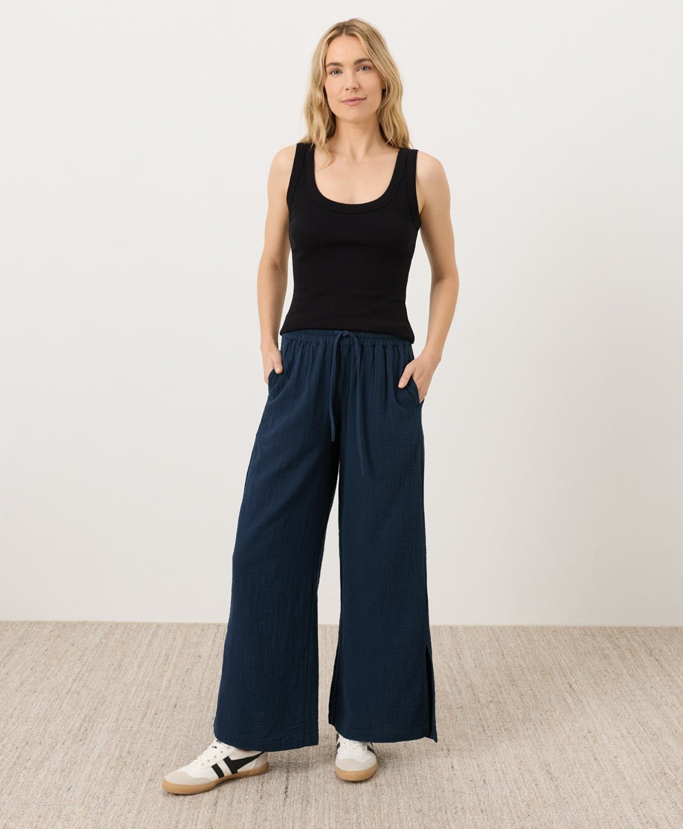 Woman wearing a black tank top and navy wide-leg pants on a plain background