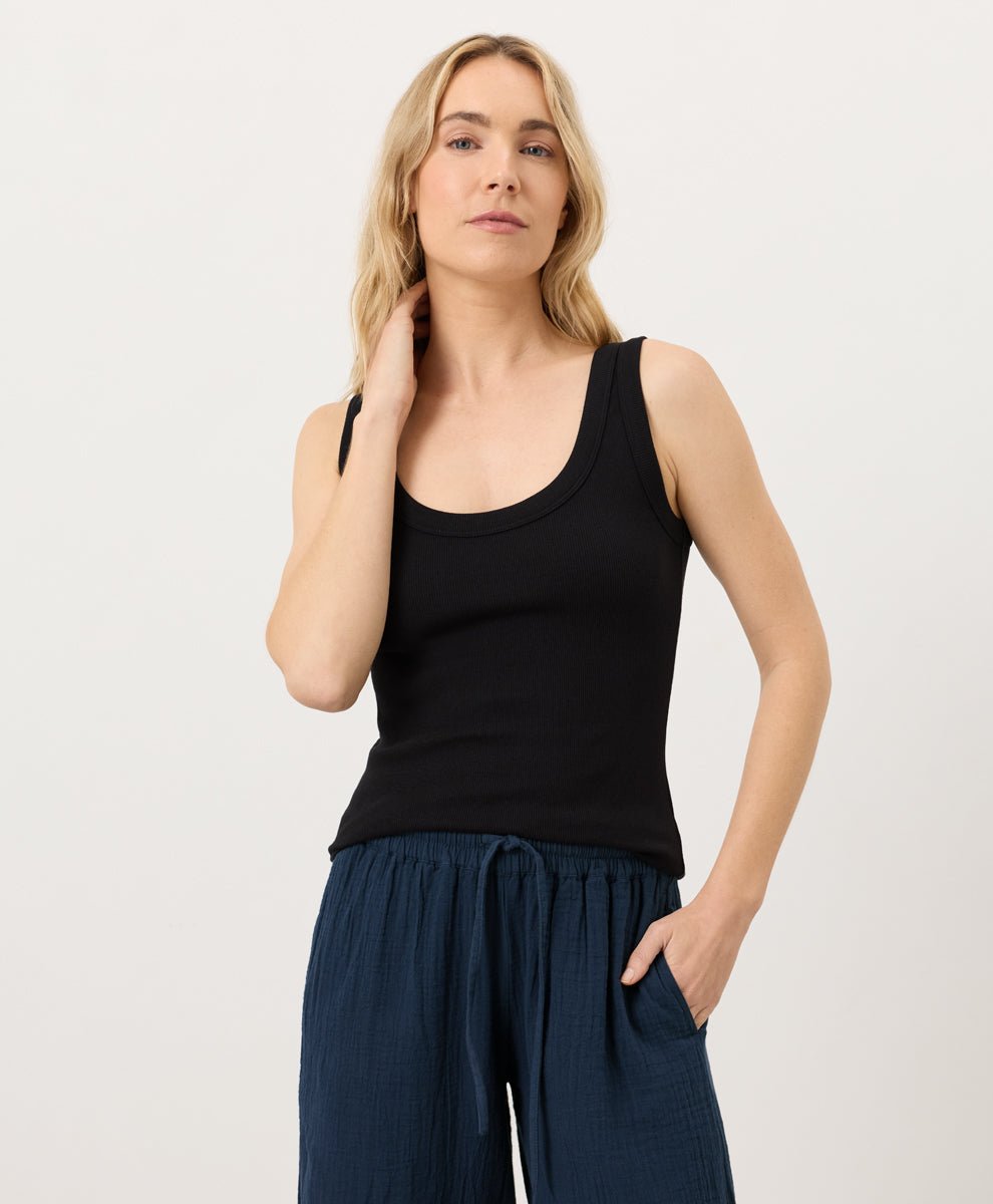 Woman wearing a black tank top and navy pants on a white background