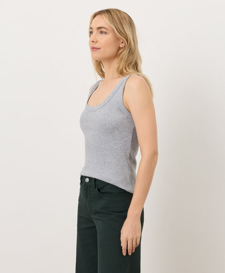 Woman wearing a gray tank top and dark pants against a white background