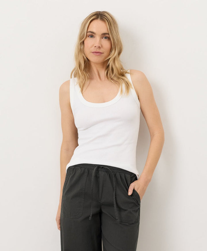 Woman wearing a white tank top and black pants against a plain background