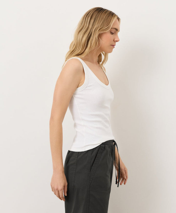 Woman wearing a white tank top and black pants against a plain background