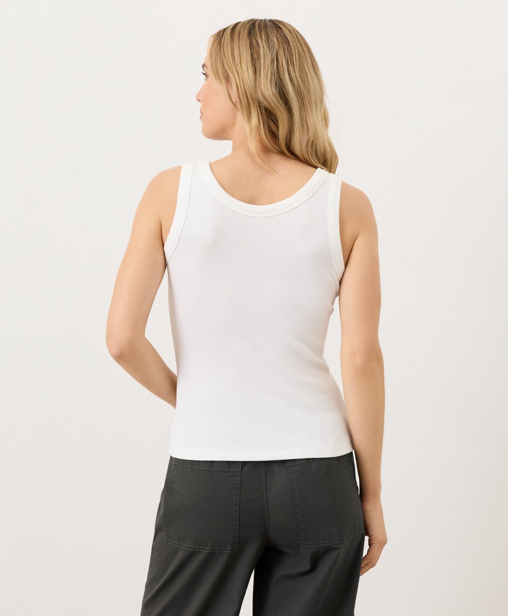 Woman wearing a white tank top and black pants on a light gray background