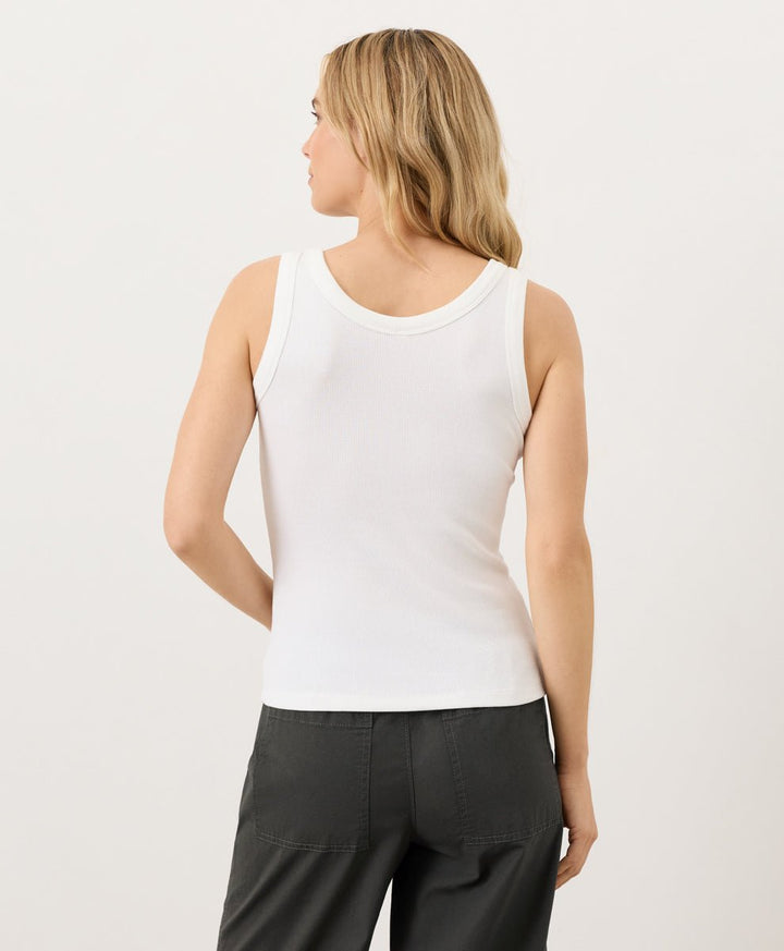 Woman wearing a white tank top and black pants on a light gray background
