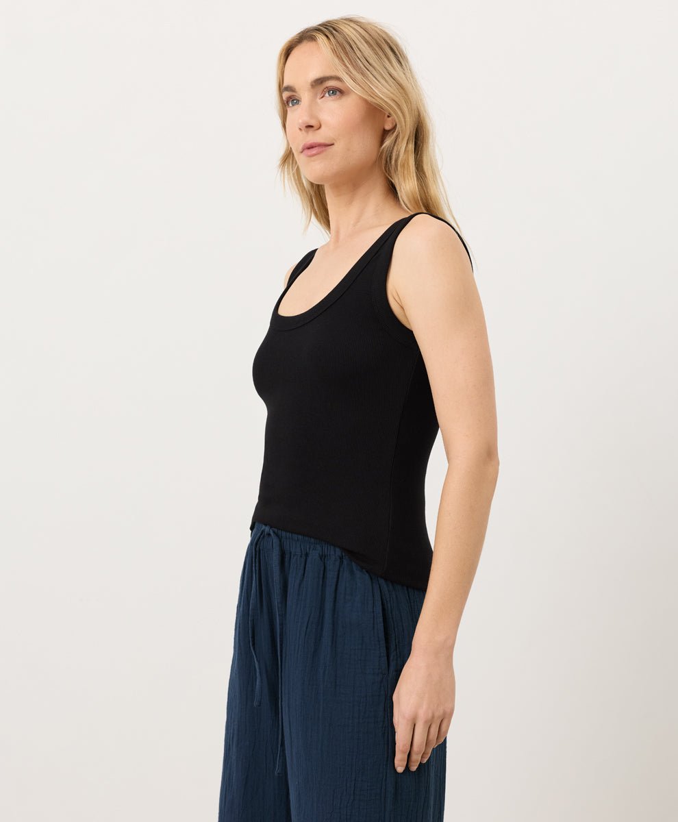 Woman wearing a black tank top and blue pants on a white background