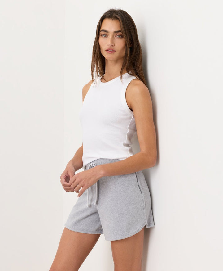Woman wearing a white Pact Organic Perfect Rib Tank and gray shorts on a plain background