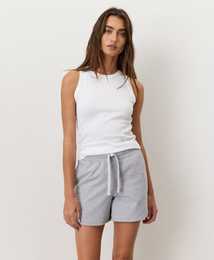 Woman wearing a white Pact Organic Perfect Rib Tank and gray shorts on a plain background