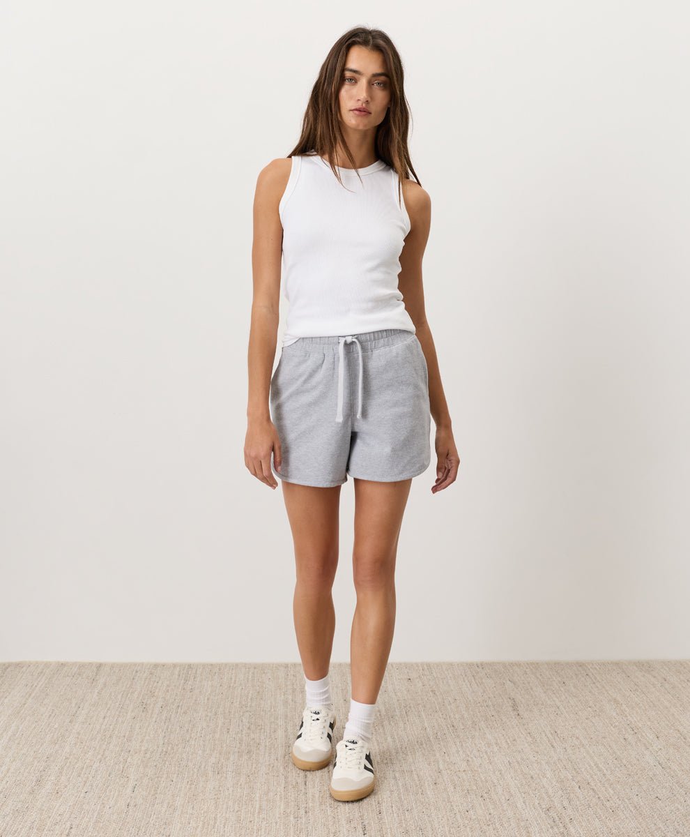 Woman wearing a white Pact Organic Perfect Rib Tank and gray shorts on a plain background