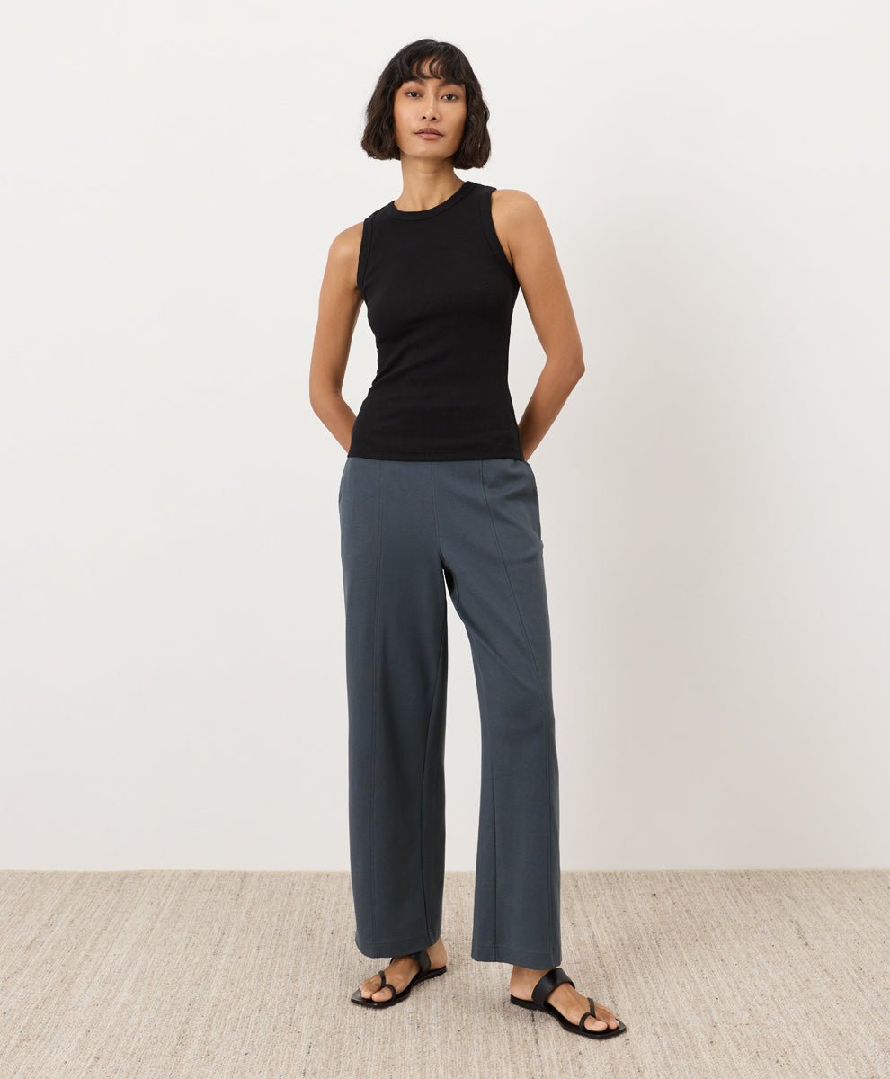 Woman wearing a black Pact Perfect Rib Scoop Neck Tank and gray pants on a white background