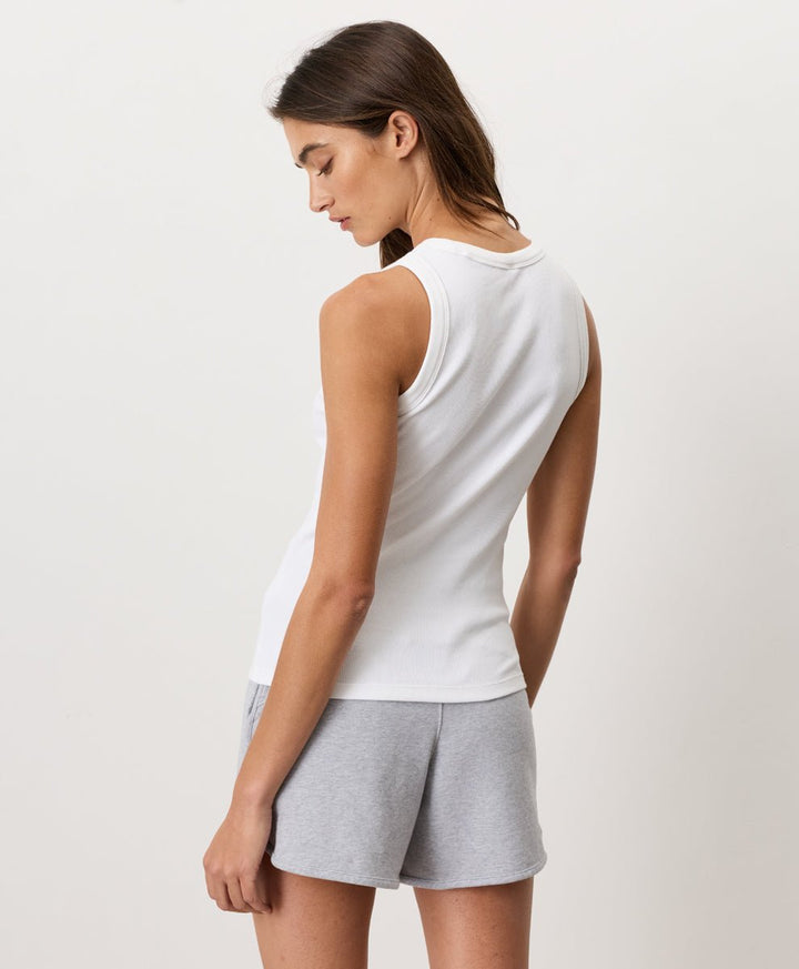 Woman wearing a white Pact Organic Perfect Rib Tank and gray shorts on a plain background