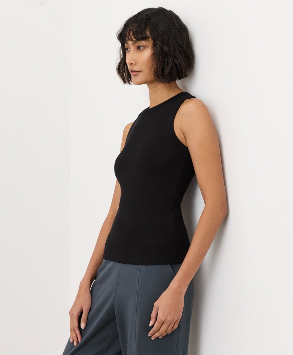 Woman wearing a black Pact Perfect Rib Scoop Neck Tank and gray pants on a white background