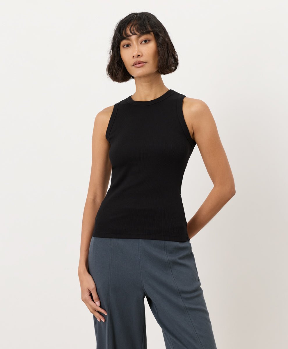 Woman wearing a black Pact Perfect Rib Scoop Neck Tank and gray pants on a white background