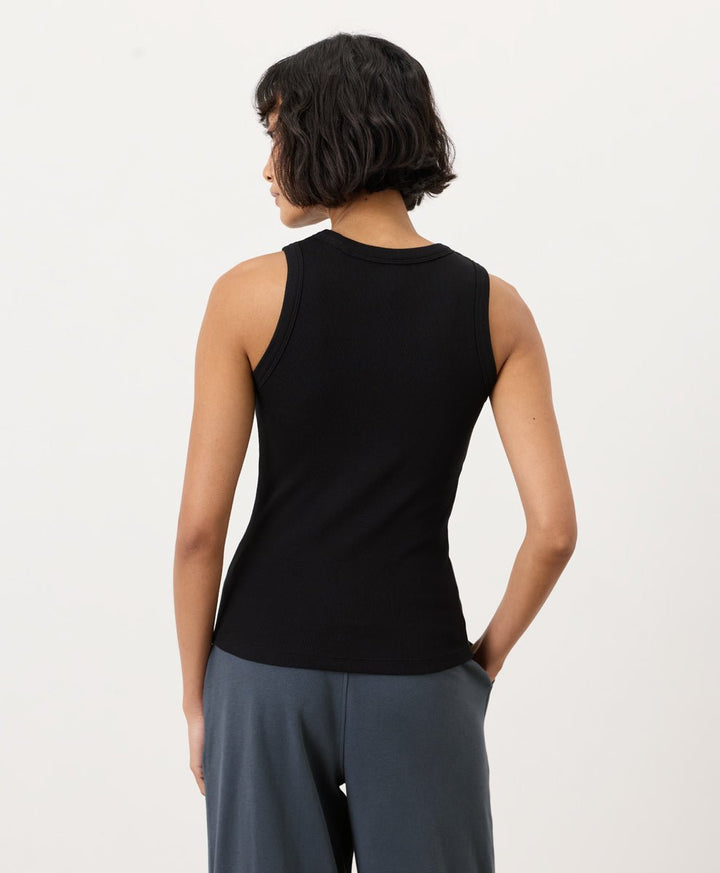 Woman wearing a black Pact Perfect Rib Scoop Neck Tank and gray pants on a white background