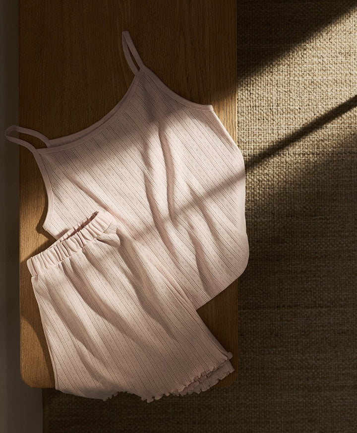 Soft pink Pact pointelle cami and shorts set on a wooden surface with soft shadows.