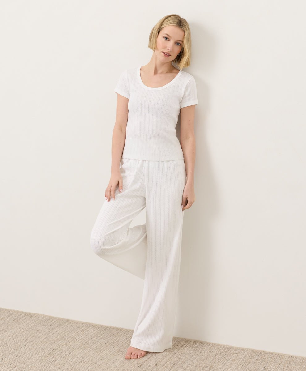 Woman wearing Pact's Organic Pointelle Scoop Neck Tee and pants in white against a white background