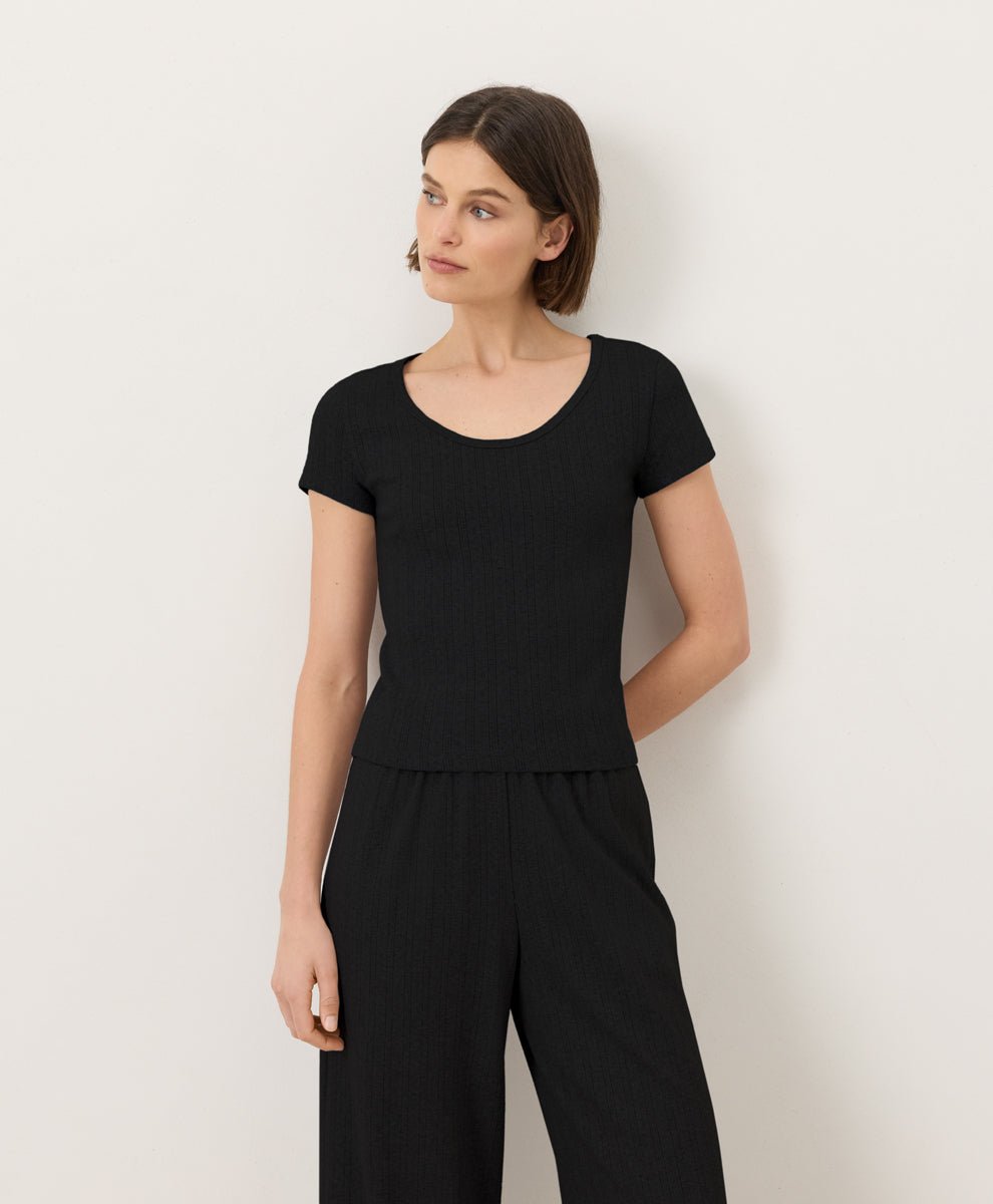 Woman wearing Pact's Organic Pointelle Scoop Neck Tee and pants in black against a white background