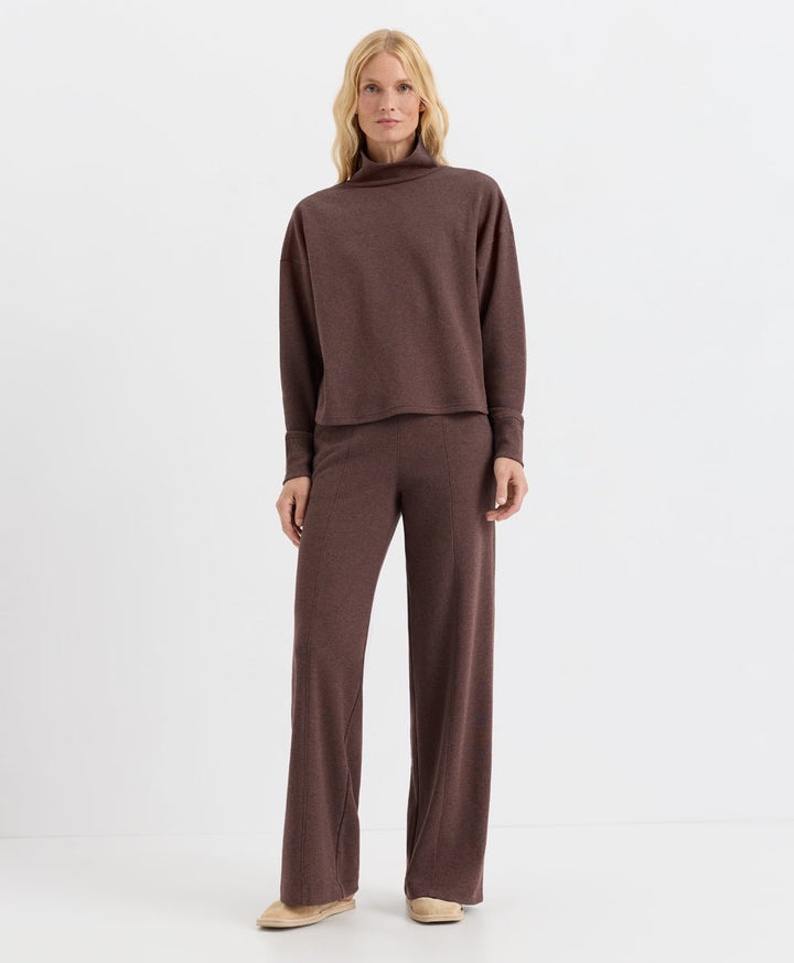 A woman modeling a matching two-piece set consisting of a long-sleeve funnel-neck top and wide-leg pants in chestnut heather, paired with beige flats, against a plain white studio background.