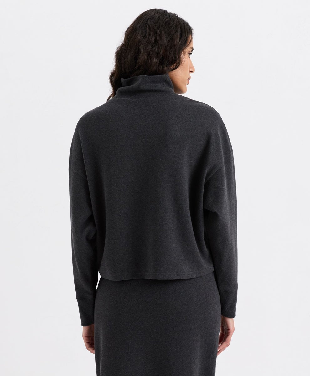 A woman shown from the back wearing a dark charcoal heather funnel neck top and a matching dark skirt against a plain light gray studio background.