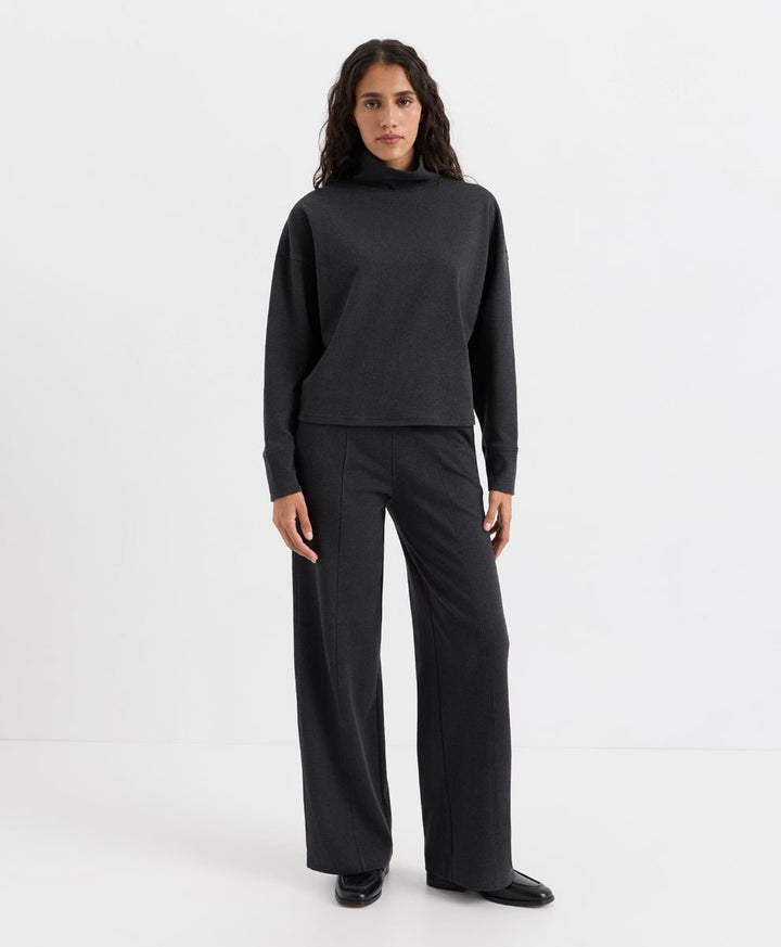 A woman modeling a dark charcoal heather knit two-piece set consisting of a long-sleeve mock-neck top and matching wide-leg trousers, photographed against a seamless white studio background.