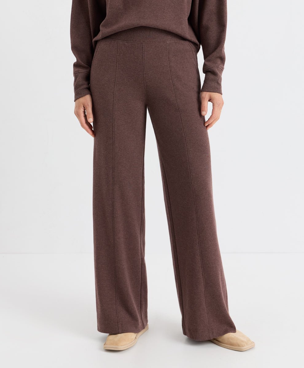 A model is shown from the waist down wearing a matching chestnut heather knit sweater and wide-leg trousers, paired with beige slip-on shoes, against a plain white studio background.