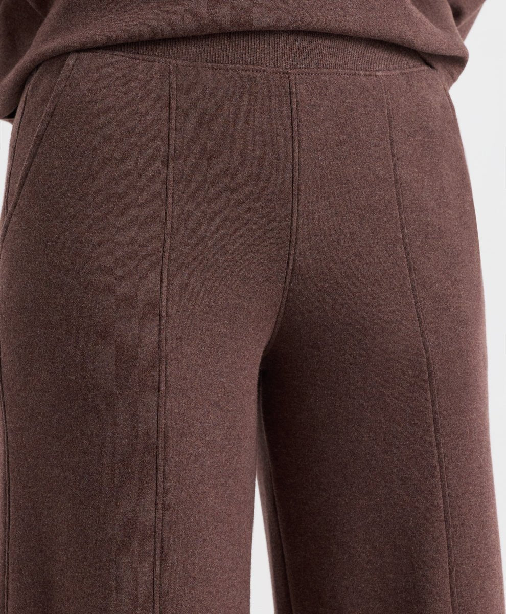 Close-up of a person wearing chestnut heather knit pants with a ribbed waistband and front seam detailing, cropped from the waist down against a plain light background.
