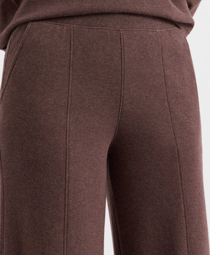 Close-up of a person wearing chestnut heather knit pants with a ribbed waistband and front seam detailing, cropped from the waist down against a plain light background.