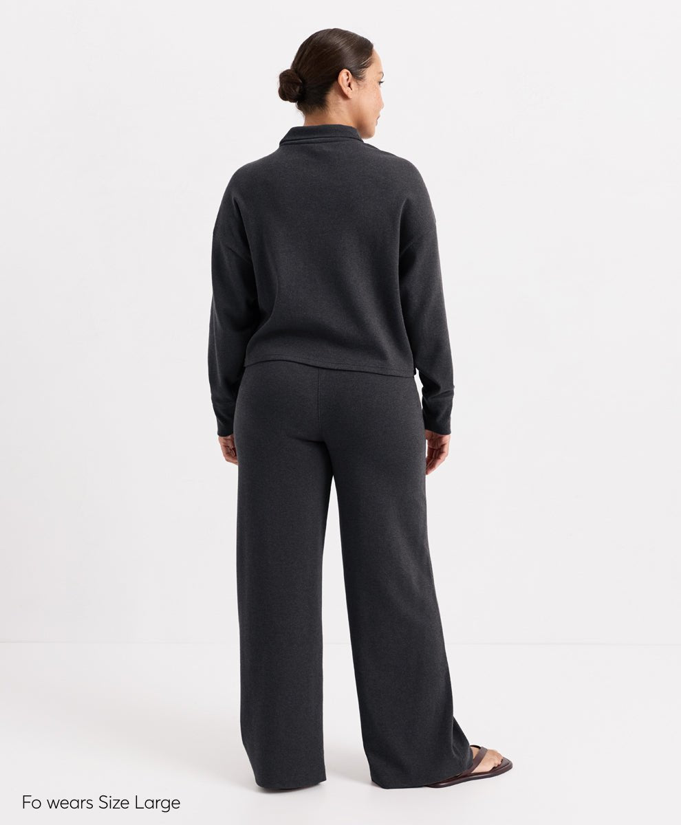 A model shown from the back wearing a dark charcoal heather mock-neck long-sleeve top and matching wide-leg trousers, photographed against a clean white studio background.
