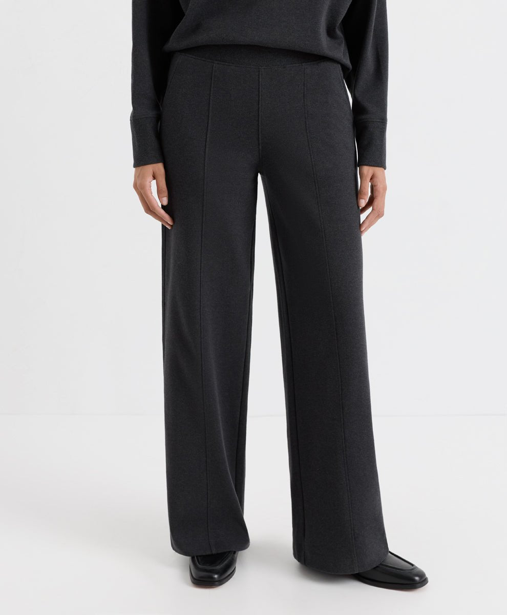 A model wearing dark charcoal heather wide-leg trousers, a matching long-sleeve top, and black leather shoes, shown from the waist down against a plain white studio background.