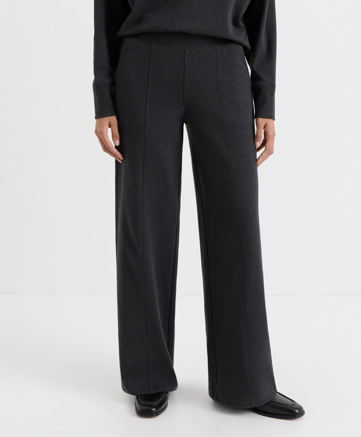 A model wearing dark charcoal heather wide-leg trousers, a matching long-sleeve top, and black leather shoes, shown from the waist down against a plain white studio background.