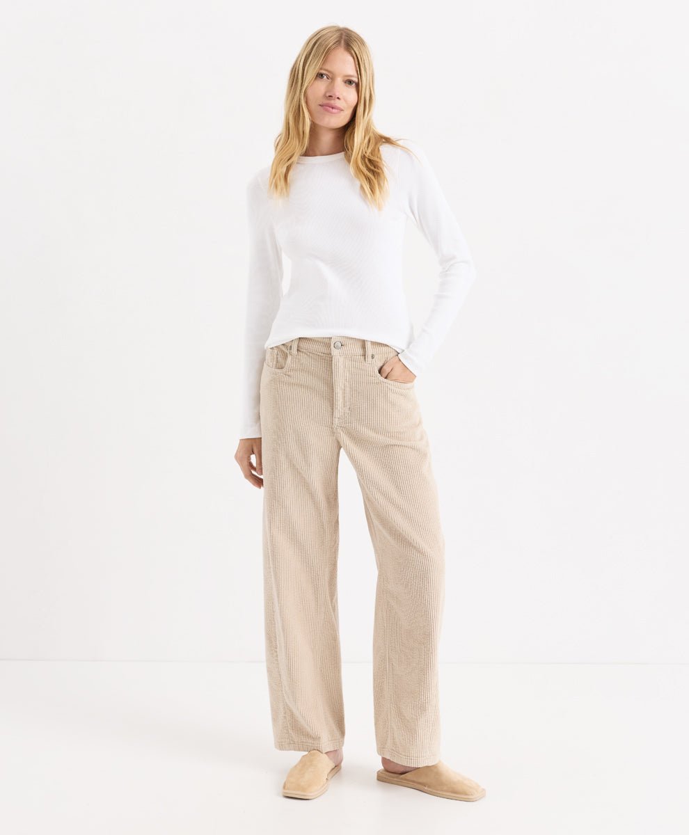 A woman modeling a white long-sleeve knit top and parchment corduroy barrel pants, paired with beige slip-on shoes, against a clean white studio background.