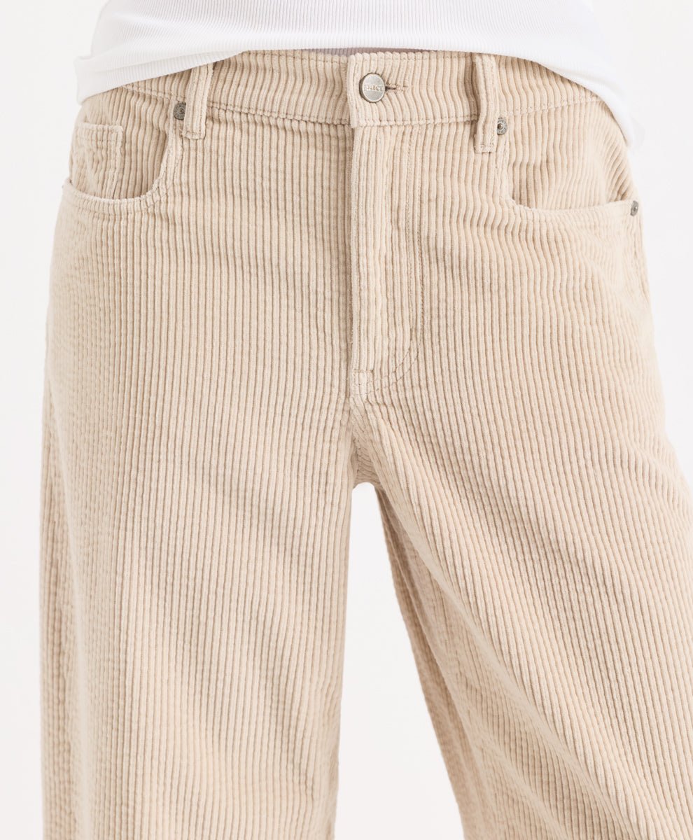 Close-up of a person wearing parchment corduroy barrel pants with a white top visible at the waist, photographed against a plain light background.