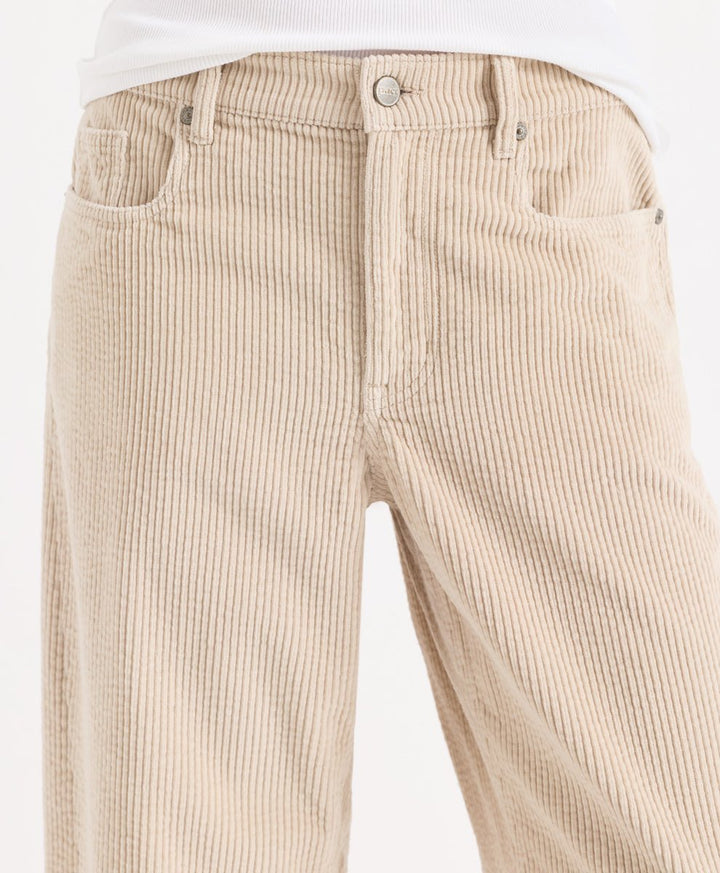 Close-up of a person wearing parchment corduroy barrel pants with a white top visible at the waist, photographed against a plain light background.