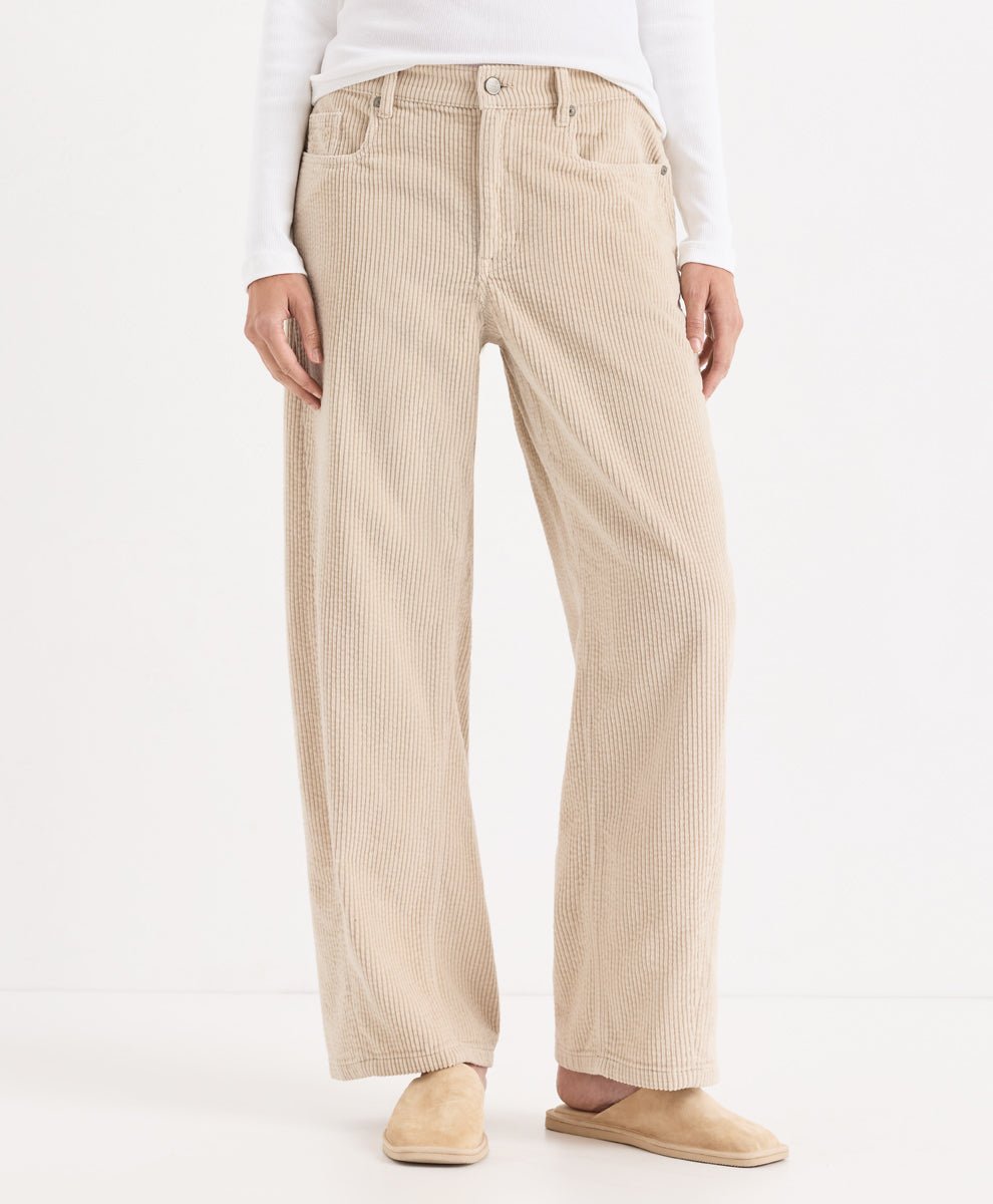 A person wearing parchment barrel corduroy pants, styled with a white long-sleeve top and beige slip-on shoes, photographed against a clean white studio background.