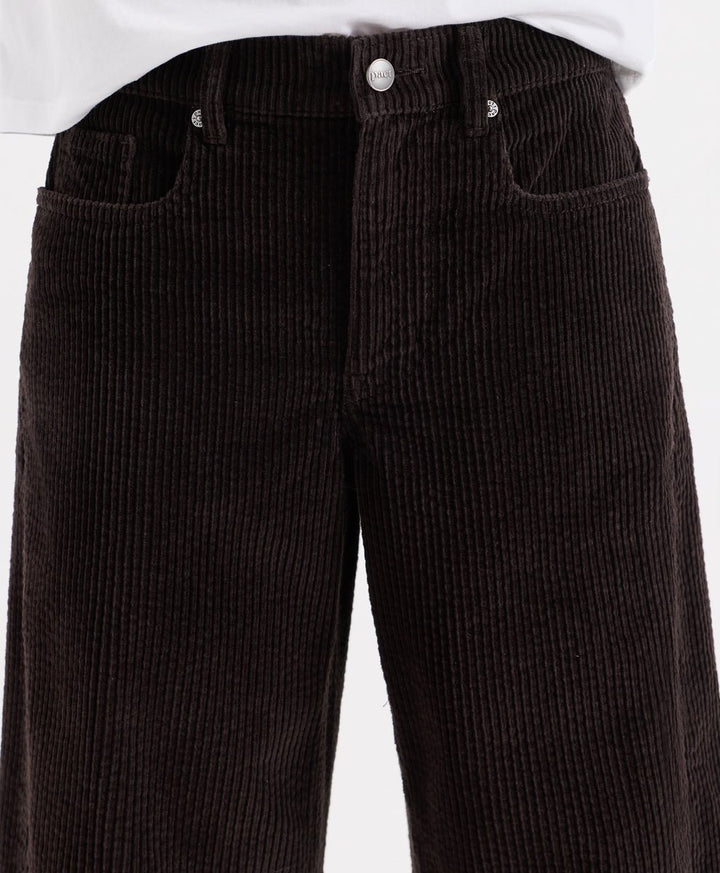 Close-up of espresso corduroy barrel pants with a white shirt hem visible at the top, showing the front waistband, button, belt loops, and side pockets.