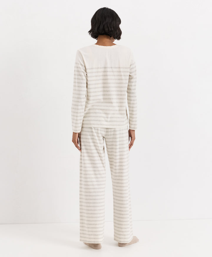 A model viewed from behind wearing a matching two-piece pajama set with a long-sleeve top and wide-leg pants, both featuring thin horizontal stripes in cream and light beige.