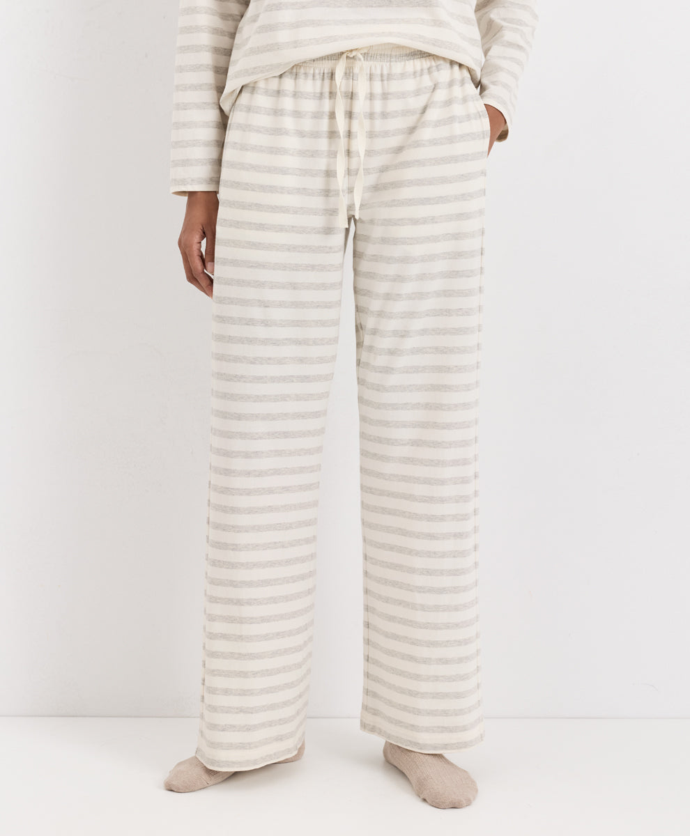 A person wearing loose, wide-leg pajama pants with thin horizontal beige and off-white stripes, paired with a matching long-sleeve top and socks, photographed against a plain light background.