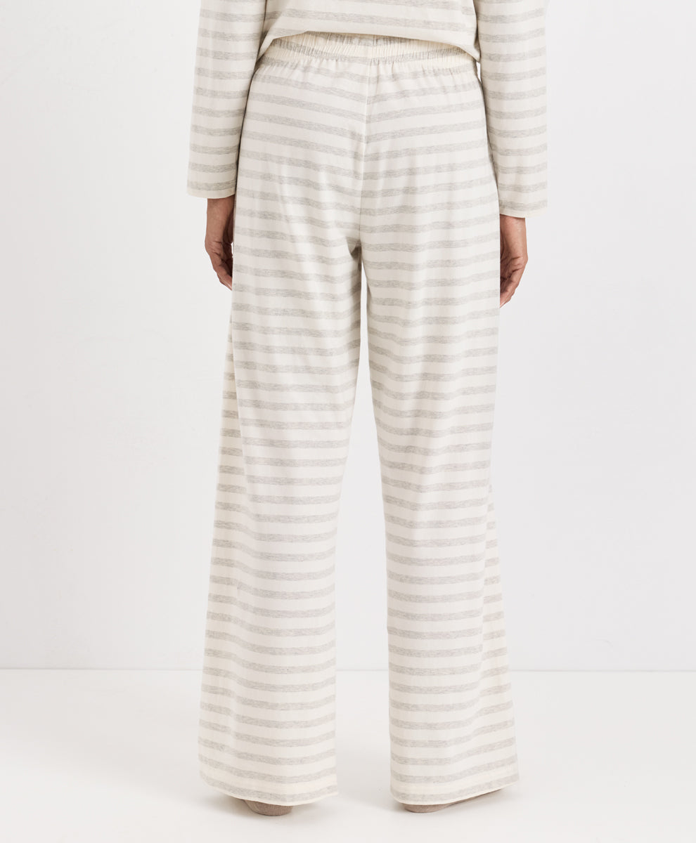 A person shown from the back wearing a matching striped lounge set, featuring wide-leg pants and a long-sleeve top in a cream and light beige stripe pattern, against a plain white studio background.
