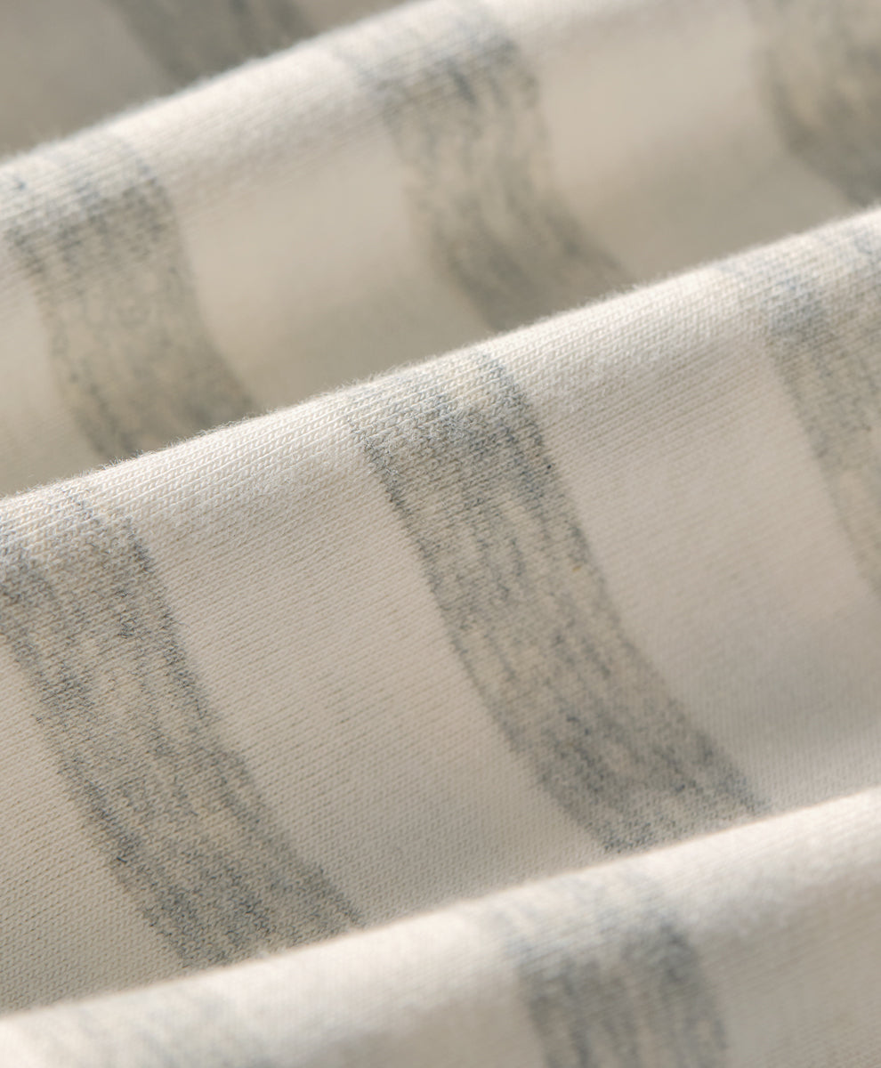 A close-up of draped fabric with soft horizontal stripes in light gray and off-white, showing the textile texture and folds.