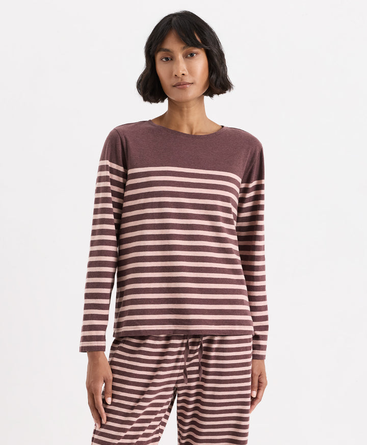 A woman modeling a matching two-piece loungewear set consisting of a long-sleeve top and pants, both featuring a horizontal stripe pattern in merlot and clay